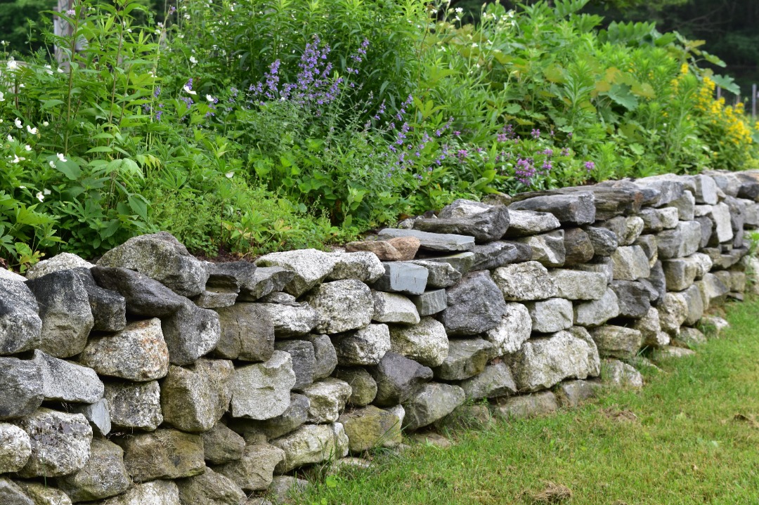 aeroscapesllc-landscape-lighting-garland A natural stone retaining wall with a plethora of vibrant plants.