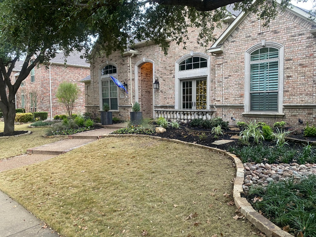 Mulched garden beds with ornamental grasses and a dry river rock feature complement a light brick home with a curved entry path.